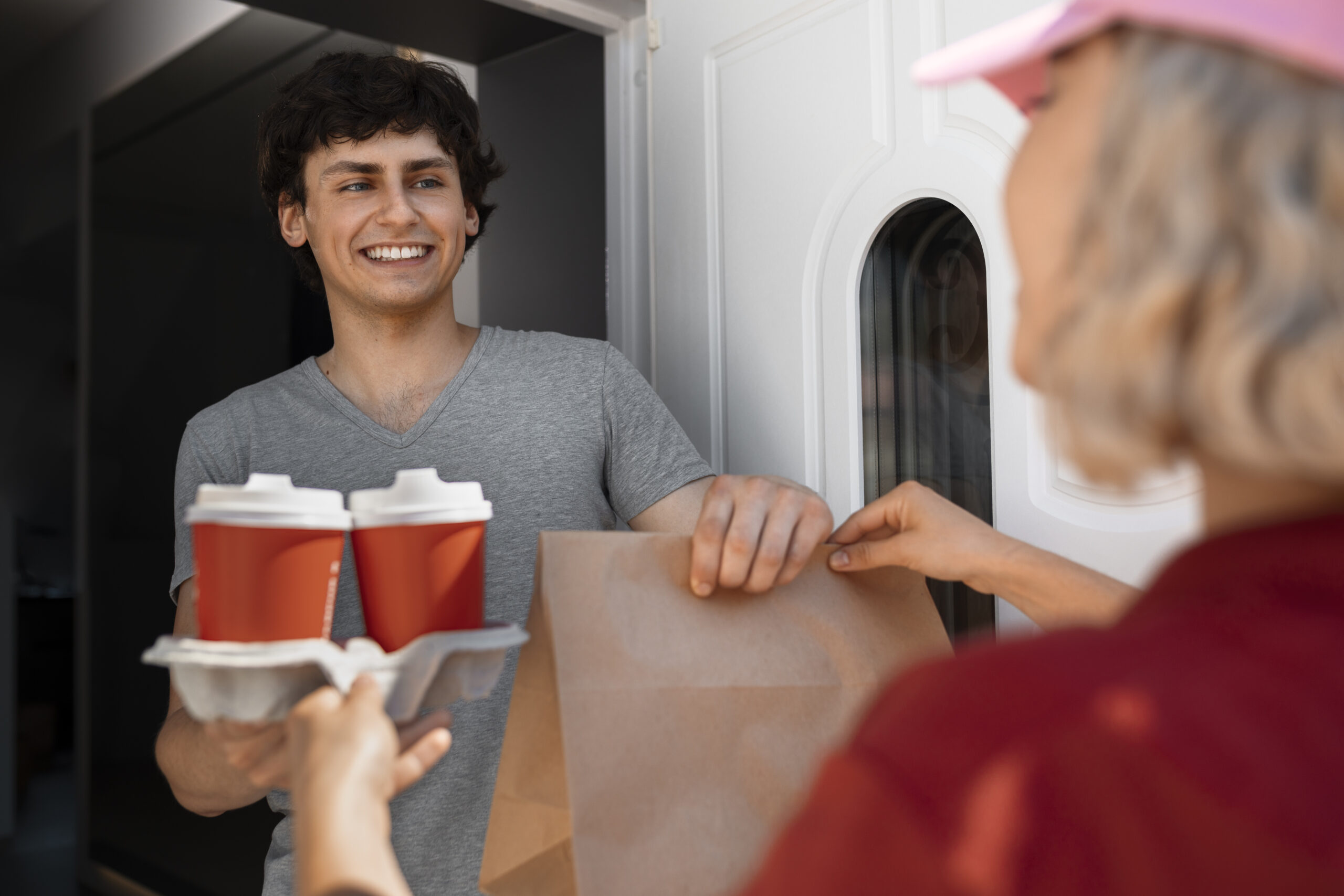 Young delivery driver handing takeout bag and coffee to customer at door – representing how restaurants beat third-party delivery fees with their own drivers and direct orders using Level POS.